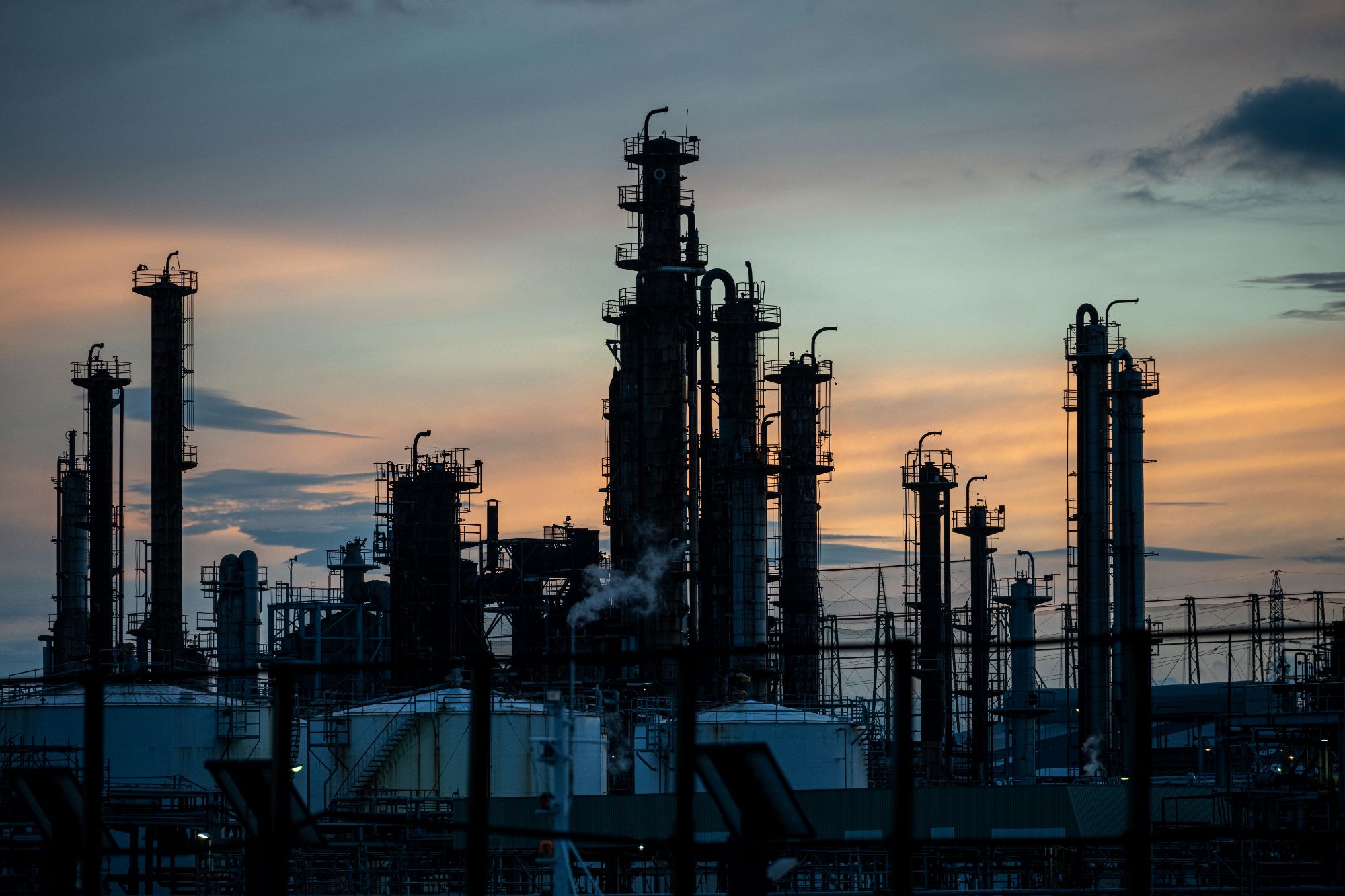 Refinería industrial al atardecer con torres de destilación y estructuras complejas, ideal para inspecciones OCA y legalización EICI