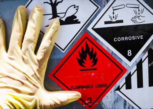 Consultoría en Prevención de Riesgos Laborales (PRL), imagen de señales de advertencia de líquidos inflamables y corrosivos con guante de protección.